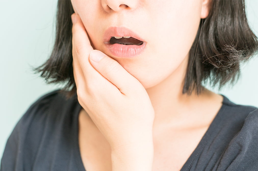 虫歯の痛みを感じ、頬に手を当てる女性
